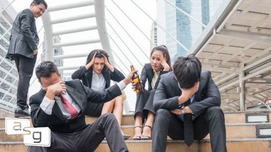 Group of professionals in business attire expressing frustration and stress outdoors, with one man offering a bottle of beer to a colleague. This image encapsulates the impact of toxic sales management habits on employee morale and wellbeing, highlighting the need for better leadership practices.