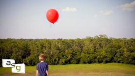 A young boy stands in a field, holding a string attached to a red balloon that floats against a backdrop of dense green trees and a clear blue sky. The image evokes a sense of simplicity and perspective, aligning with the blog's message on recognizing when a business deal isn't worth pursuing despite initial efforts and investments