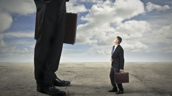 Visual metaphor comparing sales frameworks, showing a small businessman looking up at a towering figure—symbolizing the search for MEDDIC alternatives that offer greater scalability and impact.